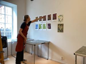 Woman wearing an apron pointing at artworks on a white wall in an art classroom
